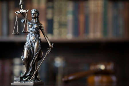 Law theme. Judge chamber. Themis and gavel on brown shining desk. Collection of legal books in the...