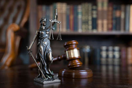 Law theme. Judge chamber. Themis and gavel on brown shining desk. Collection of legal books in the...