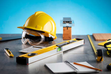 Contractor concept. Tool kit of the contractor: yellow hardhat and libella on the gray tiles and on...