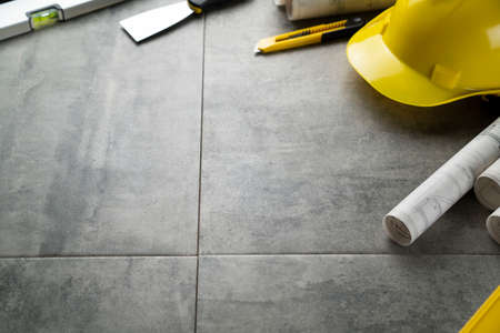 Contractor theme. Plans, tool kit of the contractor, yellow hardhat and libella. Gray tiles...