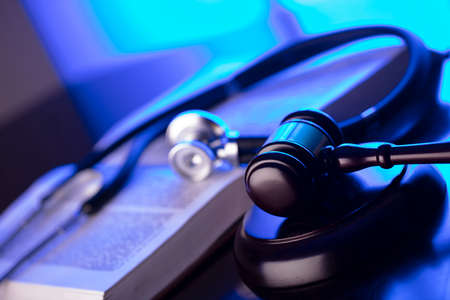 Medical law concept. Gavel, legal code and stethoscope on the glass table. Blue light.
