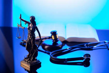 Medical law concept. Gavel, Themis, legal code and stethoscope on the glass table. Blue light.の写真素材