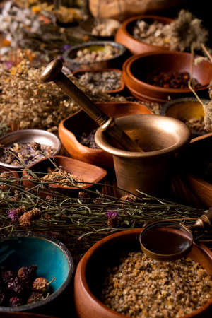 Natural medicine background. Assorted dry herbs in bowls and brass mortar on rustic wooden table.の写真素材