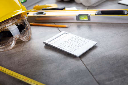 Contractor theme. Tool kit of the contractor: yellow hardhat, libella, hand saw. Plans and notebook on the gray tiles background.の写真素材
