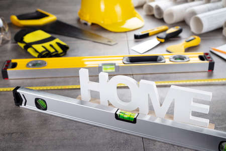 Contractor theme. Tool kit of the contractor: yellow hardhat, libella, hand saw. Plans and notebook on the gray tiles background.の写真素材