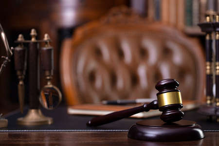 Judge office. Gavel, scale, Themis sculpture on the desk. Law books in the bookshelf.