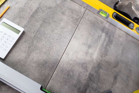 Contractor theme. Tool kit of the contractor: yellow hardhat, libella, hand saw. Plans and notebook on the gray tiles.の写真素材