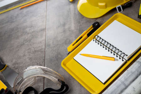 Contractor theme. Tool kit of the contractor: yellow hardhat, libella, hand saw. Plans and notebook on the gray tiles.の写真素材
