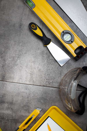Contractor theme. Tool kit of the contractor: yellow hardhat, libella, hand saw. Plans and notebook on the gray tiles.の写真素材