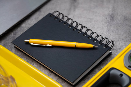 Contractor theme. Tool kit of the contractor: yellow hardhat, libella, hand saw. Plans and notebook on the gray tiles.の写真素材