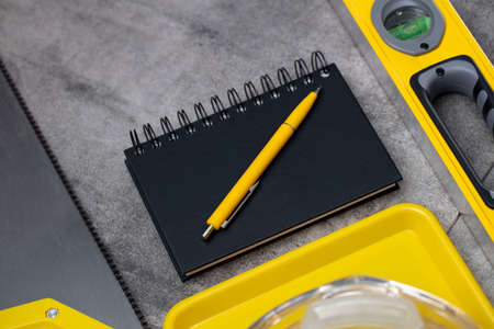 Contractor theme. Tool kit of the contractor: yellow hardhat, libella, hand saw. Plans and notebook on the gray tiles.の写真素材