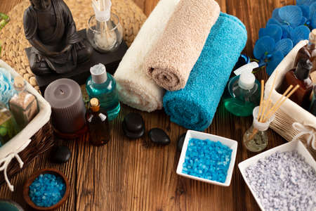Spa and wellness concept. Bottles with cosmetics, rolled up towels, bath salts and care products on wooden paneling.の写真素材