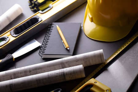 Business contraction theme. Tool kit of the contractor: yellow hardhat, libella, hand saw. Plans and notebook on the gray tiles.の写真素材
