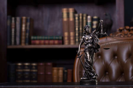 Judge office. Themis sculpture and gavel on the judge desk. Book shelf and judge chair in the background.の写真素材