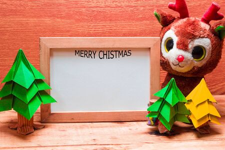 Blank whiteboard for your text on wooden background with Christmas tree, gift box and Teddy reindeer decoration image for Christmas holiday concept.の写真素材