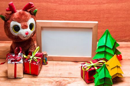 Blank whiteboard for your text on wooden background with Christmas tree, gift box and Teddy reindeer...