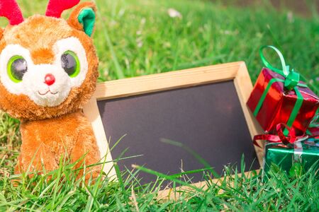 Blank blackboard for your text on lawn  background with teddy reindeer, christmas gift box for...