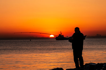 A fisherman silhouette fishing at sunset. Freshwater fishing, catch of fishの写真素材