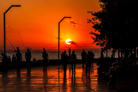 People fishing and walking at sunset on Maltepe coastal roadの写真素材