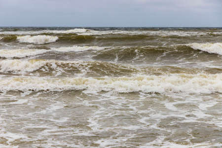 Dirty sea waves hitting the beach in stormy weatherの写真素材