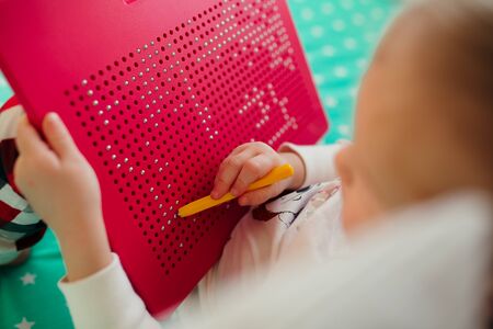 a child draws on a children's magnetic board with a yellow magnetic pen on a green cribの写真素材