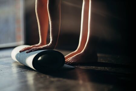 Unrecognized woman unrolling the yoga mat lying on the floor using her foot. The girl preparing for a yoga lesson or meditation at home or in the studio. Healthy lifestyleの写真素材