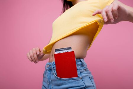 foreign passport with a ticket sticks out of the pocket of the jeans of a young girl who is going on a trip in a yellow T-shirt on a pink backgroundの写真素材
