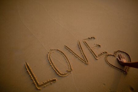 Girl's hand with an engagement ring in a heart drawn on the sand.