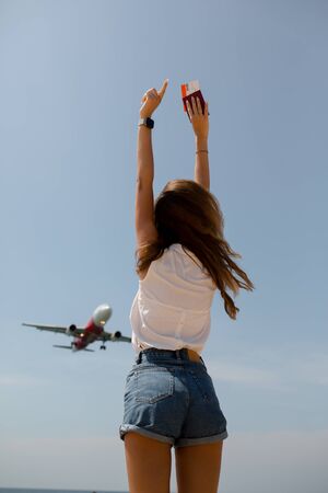 a slender girl in denim shorts and a white t shirt has her arms outstretched passport in hand near theの写真素材