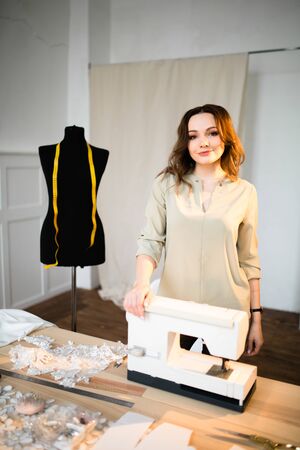 A seamstress stands next to a sewing machine.