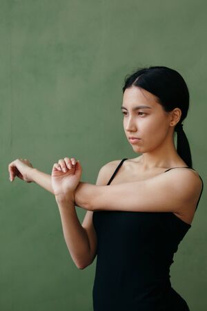 girl in black sportswear does a workout before yoga. Against the background of a green wall.の写真素材