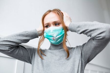 Red-haired girl in a blue mask with blood stains looks thoughtfully while waiting for a doctors consultationの写真素材