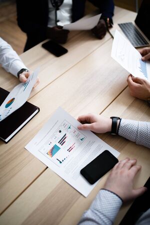 Hands of four businessmen of different nationalities with charts of company subsidiaries