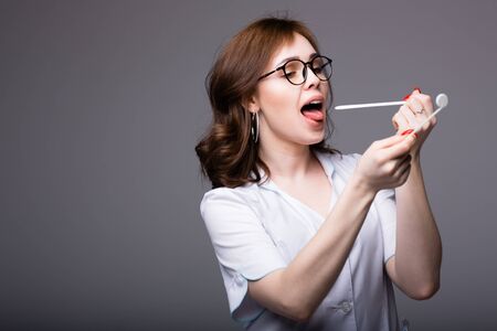 Attractive American doctor in a white coat examines his throat with a spatula and a small mirror