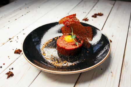 Raw tartare meat with egg yolk served on a black plate. The dish is decorated with porous toast and arugula.の写真素材