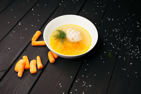 Delicate chicken soup served on a deep white plate with deep-fried chopsticks on a black wooden...