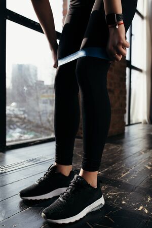Athletic woman in black sports clothes sports pulls the rubber band exercise leg musclesの写真素材