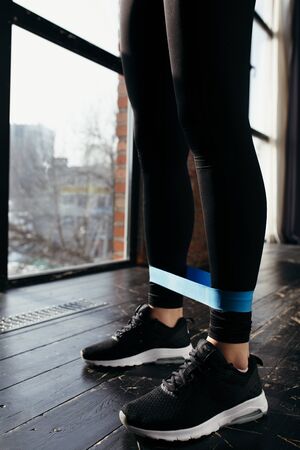 Closeup of a blue sports rubber band on the calf muscles. Black sports outfit and running shoes