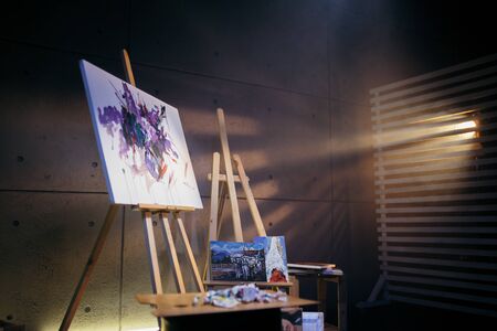 Dark art Studio where there are wooden easels, palette and abstract picture painted with watercolor paint.の写真素材
