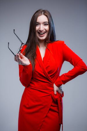An Indian woman in a red dress holds glasses near her face and laughs at the camera. Portrait photo session of a business woman.の写真素材