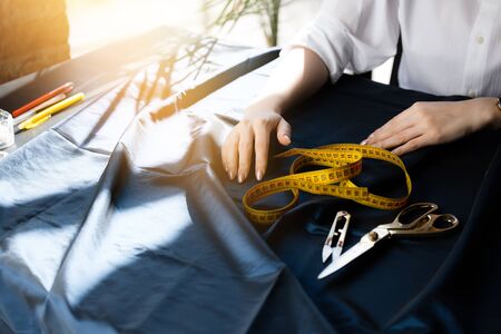 Female dressmaker's hands lie on a cut table next to scissors, a centimeter tape, a clipper for...