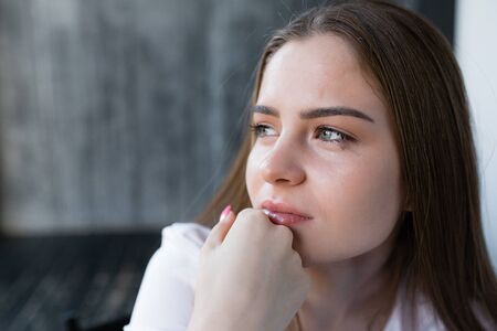 Close-up portrait of a crying girl with spreading make-up holding her hand at mouth. Stress due to...