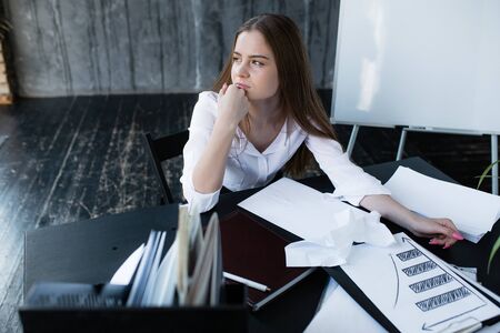 Close-up portrait of crying girl in office with spreading make-up holding her hand at mouth. Stress...