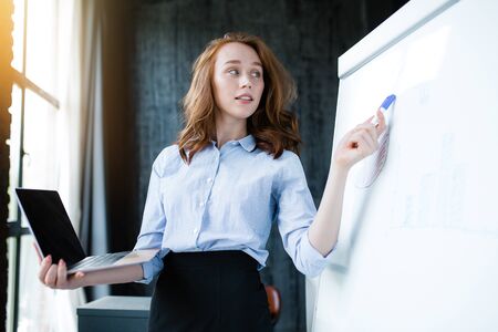 Black laptop screen for mock up. Red-haired girl conducts training and holds in her hand laptop with...
