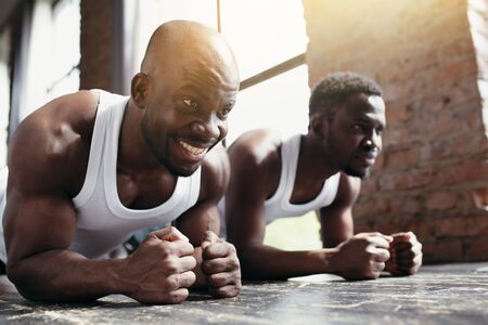 Two African-Americans in white T-shirts train the abs and back muscles while standing with their...