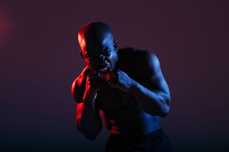 A dark-skinned, naked-chested boxer issues a cry before the fight in red-blue neon light.の写真素材