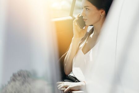 A woman in a white blouse talks to a colleague on the phone and looks out the window from the car