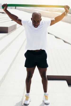 Professional black athlete from Africa is engaged in outdoor sports. Stretch elastic sports tape over the head to strengthen the hands.の写真素材