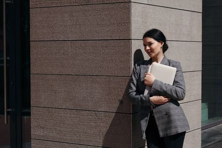 Business woman in a suit stands on the street during a break and watches people holding a laptop in her hands.の写真素材
