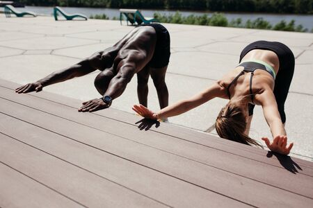 Two professional athletes do yoga exercise Adho Mukha Shvanasana, leaning his hands on the curb and pulling the tailbone upの写真素材
